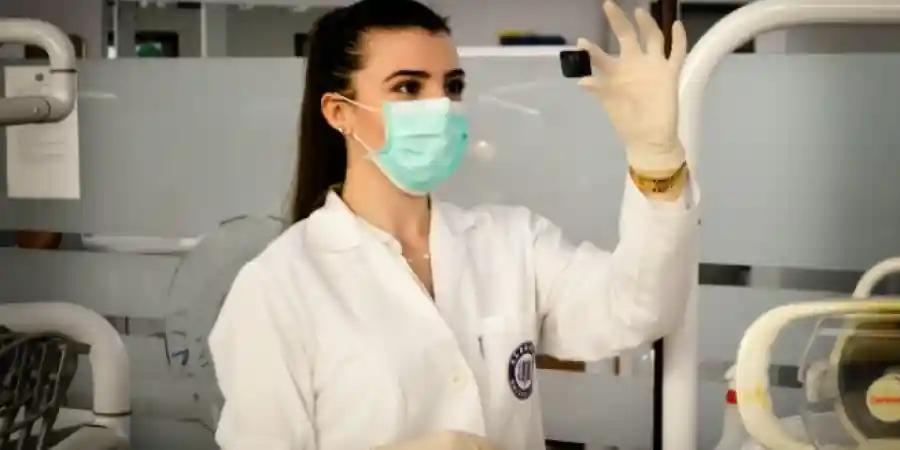 A health tech professional examines medical data on a monitor, wearing a lab coat and mask.